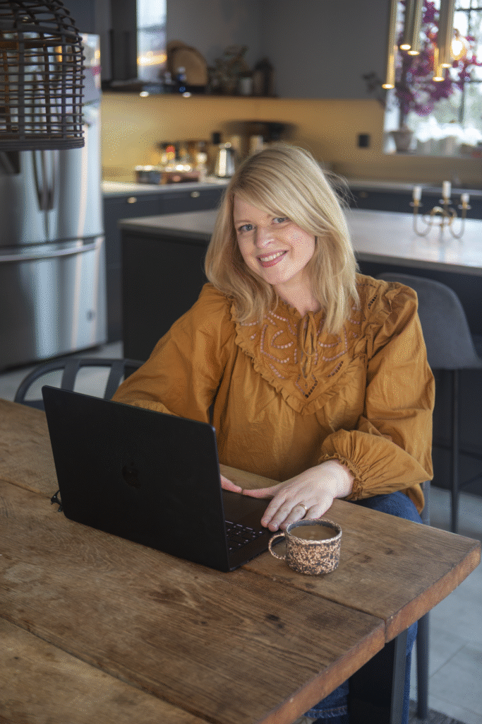 en blond kvinna i en brun tröja som sitter vid en dator som står på ett brunt bord.