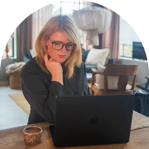 en kvinna med blont hår och glasögon som sitter och tittar på en datorskärm